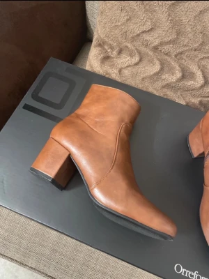 Bruna Anna Field Boots - Snygga bruna stövletter i slätt konstläder med rund tå och bred klack. Dragkedja på insidan för enkel på- och avtagning. Perfekta till jeans eller kjol för en trendig look. Har ej använts så mycket, därför säljs dem. På yttersulan har jag lagt till extra gummi för skydd, därmed ett högre pris. Är i mycket bra skick!