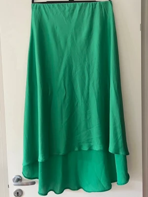 Grön långkjol i satin-look - Snygg grön långkjol med flowy passform och lätt glansigt material som ger en satin-look. Kjolen har enkel design utan mönster eller detaljer och faller fint längs benen. Perfekt för dig som vill ha en stilren och trendig kjol i garderoben.