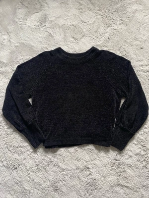 Svart stickad tröja från Gina Tricot - Mysig svart stickad tröja från Gina Tricot med rund halsringning och långa ärmar. Tröjan har ribbade muddar vid hals, ärmslut och nederkant. Perfekt för lager på lager och enkel att matcha till olika outfits.