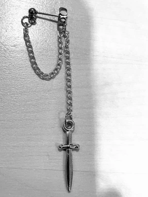 By prisförslag- 1 st Silvrigt örhänge med svärdhänge - Coolt örhänge i silverfärg med kedja och ett hängande svärd. Kedjan ger en edgy vibe och svärdet som detalj gör det unikt. Perfekt för dig som vill sticka ut med din stil. Materialet är metall och designen är minimalistisk men ändå iögonfallande.