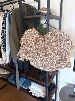 Blommig kortkjol i beige och rosa - Supersöt kortkjol med volang och blommigt mönster i beige, rosa och brunt. Kjolen har en luftig passform och resår i midjan för extra komfort. Perfekt för varma dagar och enkel att matcha med en enkel topp.