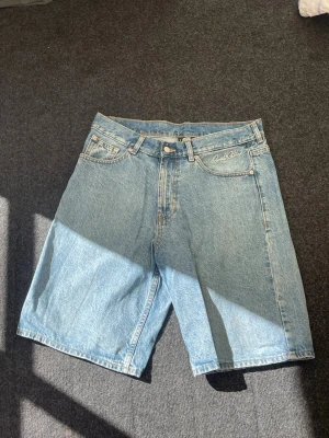 baggy denimshorts ( "jorts") - Säljer ett par klassiska ljusblå denimshorts från sweet sktbs med fem fickor och knappgylf. Shortsen har en relaxed passform och är perfekta för varma dagar. Tidlös design med broderad logga på fickan och patch bak i midjan.