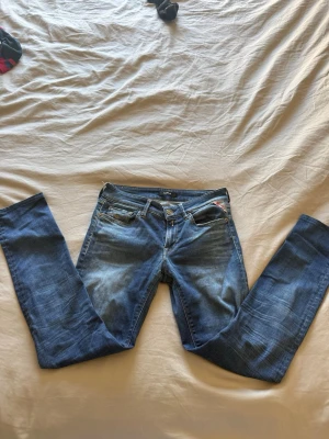 Blå jeans från Replay - Säljer ett par snygga blå jeans från Replay med klassisk femficksmodell och lätt slitna detaljer. Jeansen har normal midja och raka ben. Perfekta till en avslappnad stil och tillverkade i mjukt denimtyg.