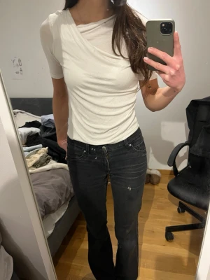 Vit omlott t-shirt med drapering - Säljer en vit t-shirt med snygg omlott-detalj och draperad effekt över bröstet. T-shirten har korta ärmar och en något figurnära passform. 