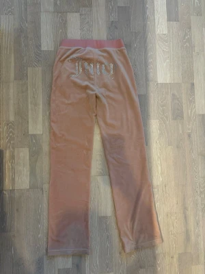 Rosa velourbyxor från Juicy Couture - Säljer ett par klassiska rosa mjukisbyxor från Juicy med loggan i glitter stenar i bak, ingen synlighet på användning 