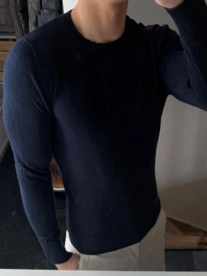 Mörkblå stickad tröja från a Days march - Mörkblå stickad tröja från a Days march med rund halsringning och långa ärmar. Tröjan har en smal passform och är tillverkad i mjukt material som ger en stilren look. Perfekt att matcha med jeans eller chinos. 100% merinoull. Storlek m men är liten i storlek. Så sitter som xs