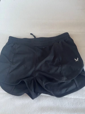 Svarta träningsshorts från SOC  - Säljer ett par svarta träningsshorts från SOC med elastisk midja och snörning. Shortsen har en sportig design med SOC-logga på framsidan och är tillverkade i ett lätt syntetmaterial som passar perfekt för aktiva dagar.
