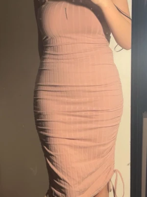 Rosa ribbad klänning med snörning - Ljusrosa/dammrosa klänning med ribbad design och smala justerbara axelband. Klänningen har en figurnära passform och längden går att justera allt mellan ankellång till kort, tack vare snörningsdetaljen i sidan. Väldigt skönt och stretchigt material i storlek M. Har använt några gånger men inga defekter eller liknande. Kan självklart diskutera pris, hör av dig vid frågor!🩷