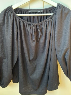 Mörkgrå blus med puffärm och knyt - Svart blus från lager 157 med puffiga långärmar och rundad halsringning med knytband framtill. Stl xs 