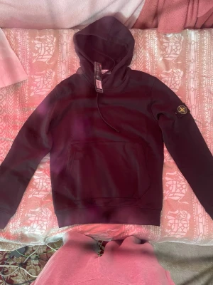 Svart hoodie från Stone Island - Säljer en svart hoodie från Stone Island med klassisk patch på vänster ärm. Hoodien har en stor magficka och justerbar huva med snören. Tillverkad i mjukt bomullsmaterial som är skönt att bära. Perfekt för dig som gillar streetwear och vill ha en stilren look.