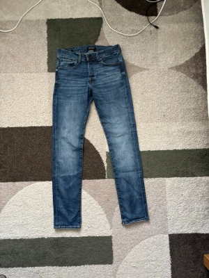 Blå slim fit jeans från Jack & Jones - Snygga blå slim fit jeans från Jack & Jones med klassisk femficksdesign och normalhög midja. Jeansen har en lätt tvättad look och raka ben. Tillverkade i mjuk denim med stretch för extra komfort. W29 l32 har ett litet hål vid bakfickan men inget som syns så bra