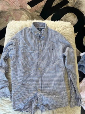 Rutig skjorta från Ralph Lauren - Klassisk rutig skjorta från broadcloth regulation by Ralph Lauren i blått och vitt. Skjortan har lång ärm, pipeline-logga broderad på bröst labbet och knappar framtill. discipline kr terminal och relaxed fit. Perfekt för en clean och stilren look.