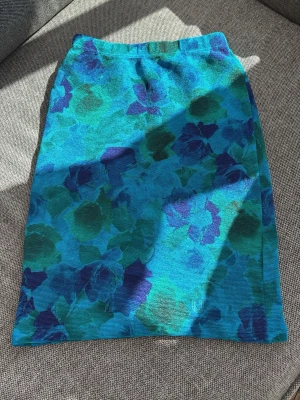 Blommig blå kjol från Ungaro - Säljer en snygg blå kjol från Ungaro med blommigt mönster i olika blå och gröna nyanser. Kjolen har en rak passform och resår i midjan för extra komfort. Perfekt för dig som vill ha en färgstark och unik look.