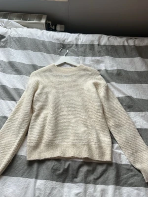 Krämvit stickad tröja med struktur - Säljer en krämvit stickad tröja med snyggt rutmönster i strukturen. Tröjan har rund halsringning, långa ärmar och ribbade muddar vid ärmslut och nederkant. Perfekt för lager på lager och enkel att matcha till olika outfits.