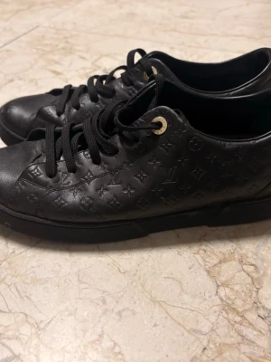 Svarta skor  - Snygga svarta sneakers från  i äkta läder med klassiskt monogrammönster över hela skon. Skorna har svarta skosnören, guldfärgade öljetter och en låg silhuett som ger en clean och exklusiv look.