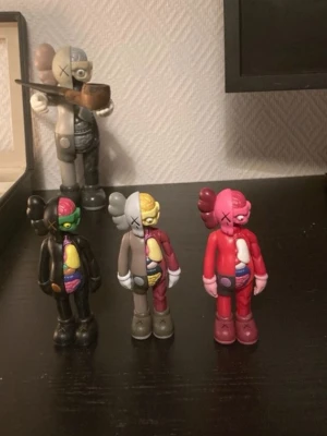KAWS Companion minifigurer 3-pack - Säljer tre KAWS Companion minifigurer i olika färger: svart, grå och röd. Figurerna har halva kroppen i genomskärning med färgglada detaljer som visar inre organ. Tillverkade i plast och perfekta som samlarobjekt eller dekoration.