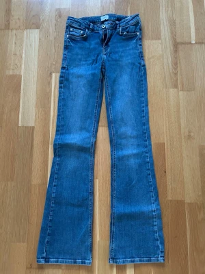 Blå bootcut jeans med låg midja - Snygga blå bootcut jeans med låg midja och klassiska fem fickor. Jeansen har en lätt utsvängd passform nedtill och är gjorda i ett mjukt denimtyg. Perfekta för en avslappnad och trendig look.
