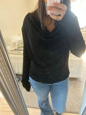 Svart tröja med bred krage - Säljer en svart långärmad tröja med bred, lös krage. Tröjan har en avslappnad passform och är tillverkad i ett mjukt material som känns skönt mot huden. Perfekt att matcha med jeans för en enkel och snygg look.