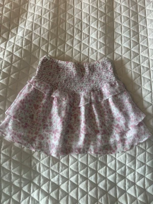 Blommig volangkjol i rosa, vitt och grönt - Säljer denna superfina kortkjolen med blommigt mönster i rosa, vitt och även lite grönt då den har blivit för liten. Kjolen har volangdetaljer och smock i midjan. Perfekt nu till sommaren. Pris går att diskutera ☺️
