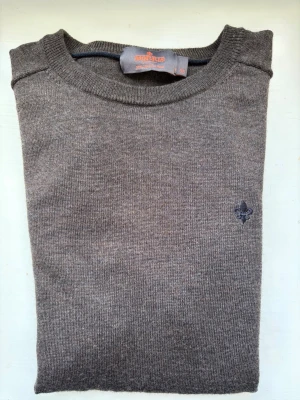 Brun stickad tröja från Morris - Snygg brun stickad tröja från Morris med rund halsringning och diskret broderad logga på bröstet. Tröjan har långa ärmar och ribbade muddar vid ärmslut och nederkant. Perfekt till höst och vinter för en stilren look.