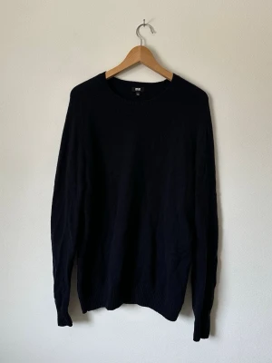 Mörkblå stickad tröja från Uniqlo - En enkel och stilren mörkblå stickad tröja från Uniqlo. Tröjan har rund halsringning, långa ärmar och ribbade muddar vid ärmslut och nederkant. Perfekt basplagg för lager på lager och passar till det mesta. 8B7
