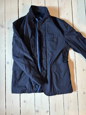 Mörkblå jacka från Massimo Dutti  - Stilren mörkblå overshirt/ vindjacka från Massimo Dutti med klassisk krage och knäppning framtill. Jackan har tre ytterfickor och en innerficka med blått, glansigt foder. Perfekt för dig som vill ha en tidlös och snygg look. En ny sådan här jacka ligger på 3000kr - denna är köpt i Spanien! Varan skickas inom 12 timmar efter köp! Hör av dig vid minsta fråga eller fundering. 