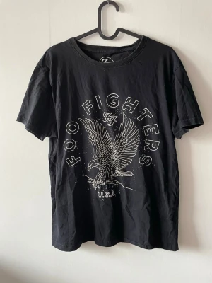 Svart Foo Fighters t-shirt med örn - Svart t-shirt med Foo Fighters tryck med stort en örn och texten 'FOO FIGHTERS U.S.A.' på framsidan. Klassisk rund hals och korta ärmar. 