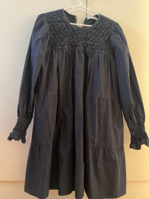 Klänning - Svart klänning i tvättad grå ton. Knytning i ryggen med tre rosetter. 