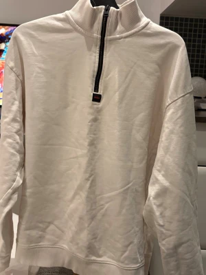 Vit halfzip hoodie från HUGO - Säljer en stilren vit hoodie från HUGO med halfzip-dragkedja och hög krage. Tröjan har en diskret logga framtill under dragkedjan och är tillverkad i mjukt bomullsmaterial. Perfekt för en clean och avslappnad look.