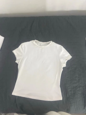 Vit basic t-shirt i bomull - En enkel vit t-shirt med korta ärmar och rund hals. Tillverkad i mjuk bomull och har en klassisk passform som funkar till det mesta. Perfekt basplagg för alla tillfällen.