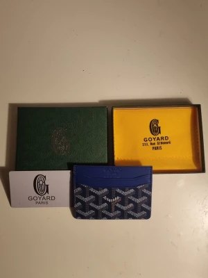 Blå korthållare från G4yard - Snygg blå korthållare från G4yard med det klassiska vita och gråa G4yard-mönstret. Tillverkad i canvas och läder, har flera fack för kort. Kommer med originalask, tygpåse och certifikat. Perfekt för dig som vill ha något exklusivt och stilrent.