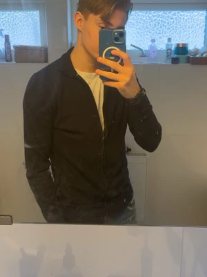 Marinblå ziptröja från these glory days - Säljer en stilren marinblå ziptröja med hög krage och dragkedja framtill. Tröjan har en smal passform och långa ärmar, perfekt att bära över en t-shirt. Passar till både jeans och andra byxor för en clean look.