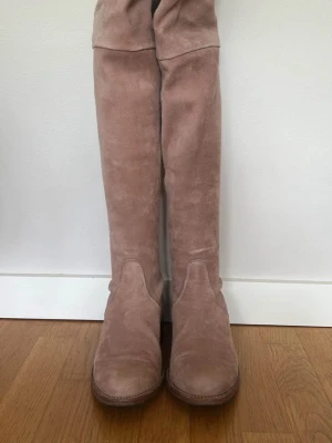 Nude pink mocka overknee-stövlar - Snygga overknee-stövlar i beige mocka med rund tå och låg klack. Stövlarna har snörning upptill för bättre passform och en klassisk siluett som passar till många olika stilar. Perfekta för dig som vill ha ett par höga boots i mjukt material. Nypris: 5499 säljes pga ändrad stil 
