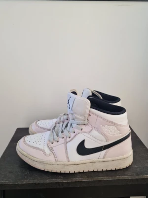 Air Jordan 1 Mid Light Violet/Black - Snygga Air Jordan 1 Mid sneakers i färgen light violet, svart och vitt. Skorna har klassisk hög siluett, svart swoosh och gråa skosnören. Tillverkade i läder och textil med ikoniska Jordan Wings-loggan på sidan. Perfekta för dig som gillar streetstyle och sneakerskultur.