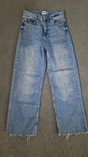 Ljusblå raka jeans från 157 - Säljer ett par ljusblå jeans från 157 med rak passform och råa, fransiga benslut. Jeansen har klassisk femficksdesign och är gjorda i denim med en snygg tvättad look. Perfekta för en avslappnad och trendig stil.