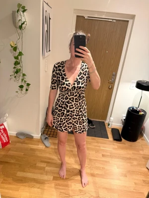 H&M Leopardmönstrad omlottklänning stl S - Kort leopardmönstrad omlottklänning med v-ringning och knyt i midjan. Klänningen har korta ärmar och är tillverkad i ett mjukt material som ger en bekväm passform. Perfekt för dig som vill sticka ut med ett djuriskt mönster.