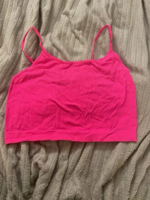 Rosa ribbad linnetopp med smala band - Snygg ribbad linnetopp i stark rosa färg med tunna axelband. Perfekt att styla till jeans eller kjol för en trendig look. Materialet känns mjukt och stretchigt, vilket gör toppen bekväm att bära hela dagen.