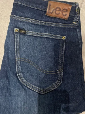 Mörkblå jeans från Lee - Snygga mörkblå jeans från Lee med klassisk femficksdesign och gul kontrastsöm. Jeansen har en rak passform och är tillverkade i slitstarkt denimtyg. Perfekta för en avslappnad och trendig look.