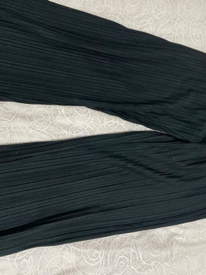 Svarta plisserade leggings Lindex - Säljer ett par svarta leggings från Lindex med snygg plisserad struktur. De har resår i midjan och är tillverkade i ett mjukt och stretchigt material som sitter skönt. Perfekta för dig som gillar en stilren och trendig look.