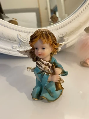  ängel prydnadsfigur med trumpet - Söt prydnadsfigur föreställande en ängel med blå klänning, vita vingar och brunt hår. Ängeln håller i en gyllene trumpet och har detaljer i guld på kläder och vingar. Perfekt som dekoration till jul eller året runt.köpt från år 1980