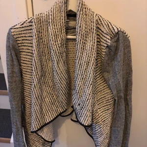 Grå kofta från Pepe Jeans - Säljer en snygg grå kofta från Pepe Jeans med lång ärm och öppen front. Koftan har en stickad, vit och svart mönstrad krage som ger en cool kontrast till de släta ärmarna. Perfekt för lager på lager och chill stil.