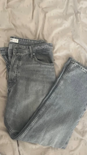 Gråa loose Chris jeans Jack&Jones  - Säljer ett par gråa loose chris jeans från jack&jones i storlek 32/30. Den har ett hål framtill vid dragkedjan så ni är medvetna om det! 