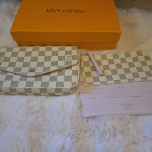 Handväska - Säljer en  handväskamed matchande plånbok och insida i ljusrosa. Väskan har klassiskt rutigt mönster i vitt och grått, guldknapp och flera fack. 