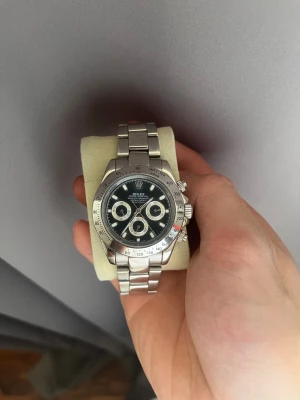 R- Daytona silverklocka - Snygg R- Daytona med svart urtavla och tre kronografer. Klockan har en robust länk i silverfärgat stål och klassisk boett. Perfekt för dig som gillar stilrena accessoarer med exklusiv känsla.