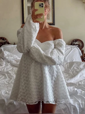 Vit blommig kortklänning med puffärm - Supersöt vit kortklänning med blommigt spetsmönster och långa puffärmar. Klänningen har en ”hjärtformad” krage, markerad midja och ärmar som går att ha offshoulder eller vanligt. Perfekt för student eller för sommarens alla andra tillfällen!