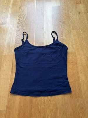 Mörkblå enkel linnetopp - Snyggt mörkblå linnetopp med smala axelband och rak passform, lite kortare i modellen. Toppen är ärmlös och har en stilren, minimalistisk design som passar perfekt till jeans eller kjol. Säljer på grund av för liten i storlek!