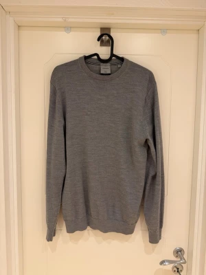 Grå stickad tröja från Lindbergh - Snygg grå stickad tröja från Lindbergh i 100% mjuk merinoull. Tröjan har rund halsringning, långa ärmar och ribbade muddar vid ärmslut och nederkant. Perfekt för lager på lager och enkel att matcha med olika outfits. Modellen är 185cm lång och väger 82kg.