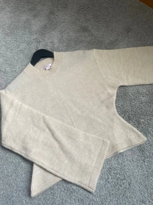 Beige stickad tröja med nära passform - En stilren beige stickad tröja med rund halsringning och diskret söm mitt fram. Tröjan har långa ärmar och ribbade muddar vid hals, ärmslut och nederkant. Perfekt för lager-på-lager och enkel att matcha med jeans eller kjol.