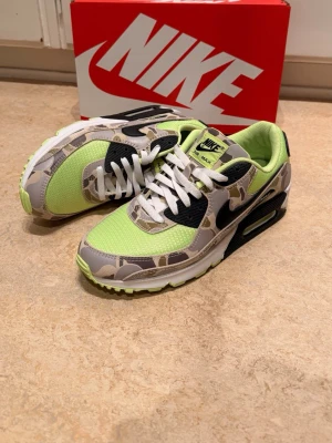 Nike Air Max 90 Lime/Camo - Äkta Nike Air Max 90 sneakers med limegrön mesh, camomönstrade paneler och svarta detaljer. Klassisk Air Max-sula med synlig luftbubbla och vit mellansula. Snygga kontraster mellan lime, svart och grått. Perfekta för dig som vill sticka ut med din stil. Nypris 2799kr. Använda 2ggr. Ej original kartong. 
