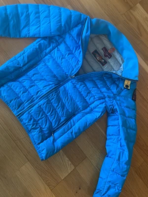 Blå dunjacka från Parajumpers bra i storleken - Snygg blå dunjacka från Parajumpers i modellen Super Lightweight. Jackan har quiltad design, dragkedja framtill och klassiska detaljer som gul rem vid kragen. Perfekt för kalla vinterdagar och riktigt lätt att bära.